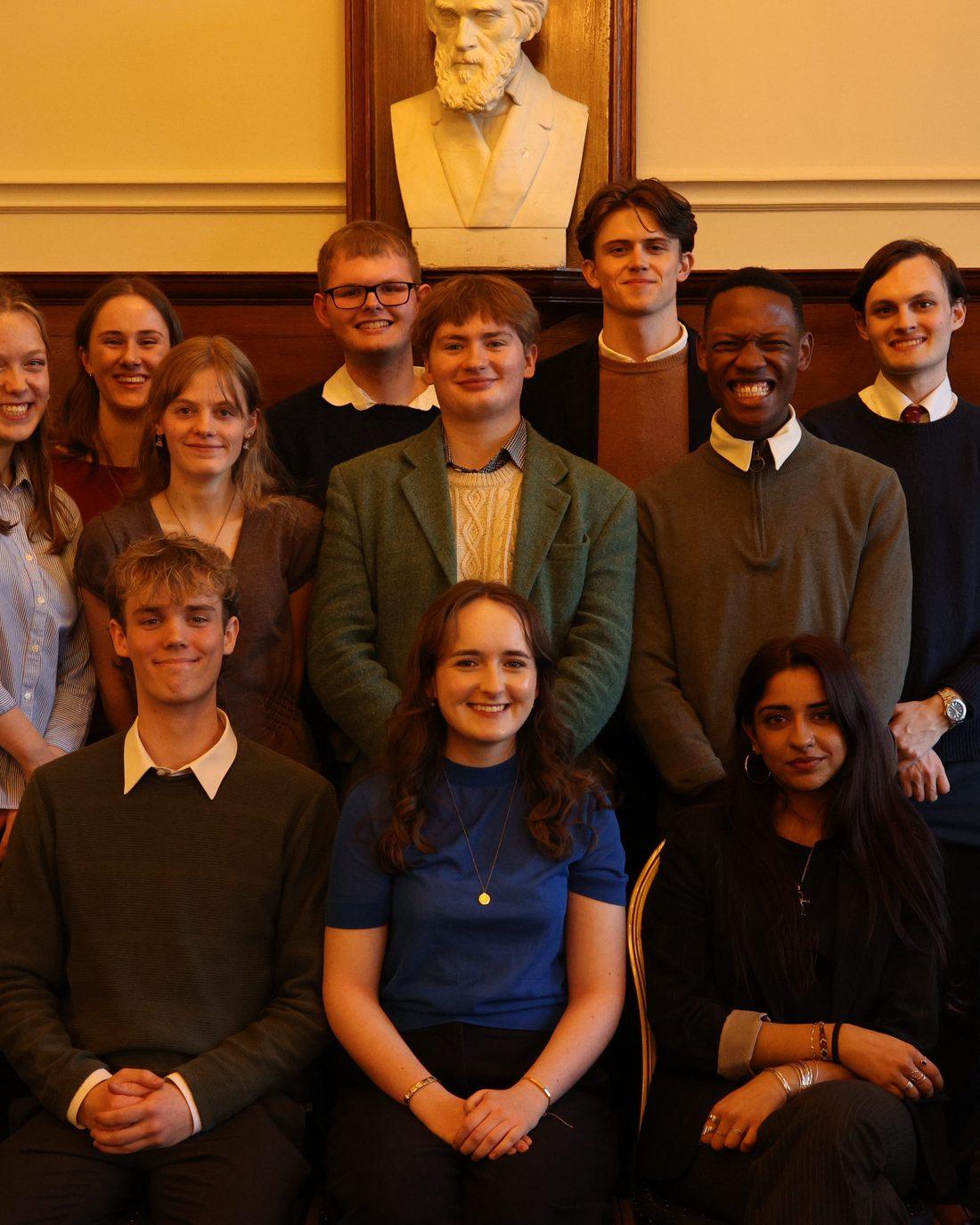 The committee gathered beneath the marble bust, a second frame from the same sitting