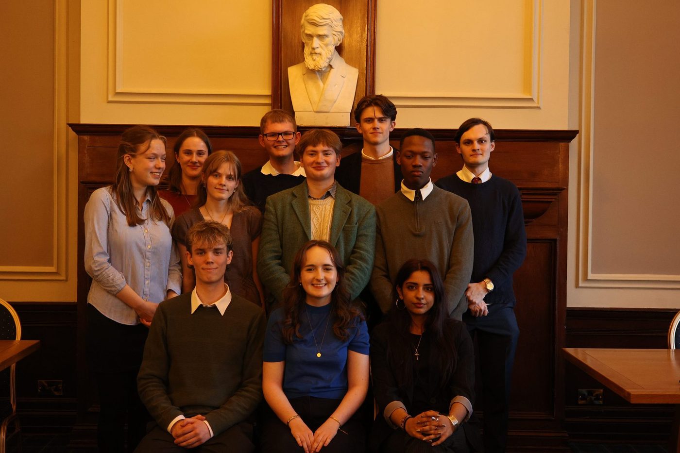 The committee indoors in a wood-panelled room, beside a marble bust