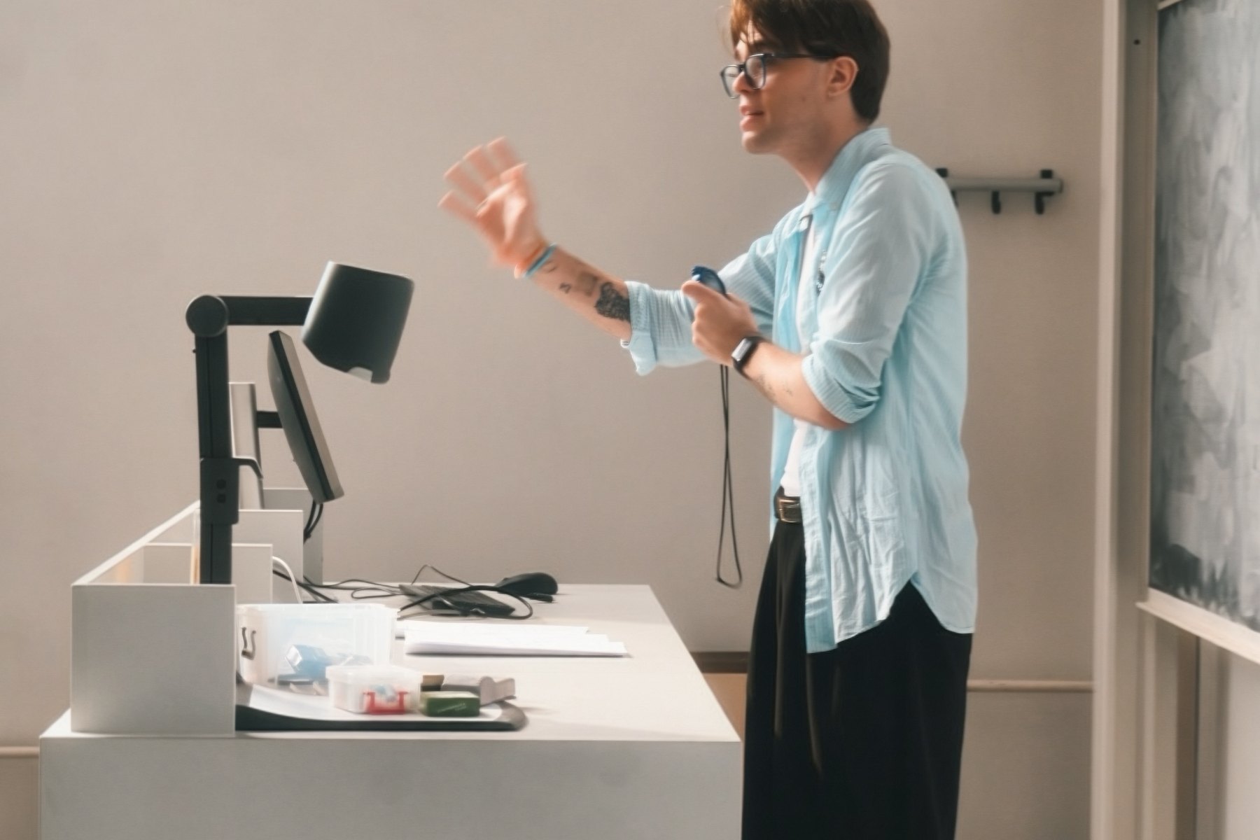 A member speaking beside a desk at the front of a teaching room